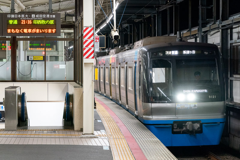 印西牧の原行の下り発車標に対して入線してくるのは下り新鎌ヶ谷行という妙